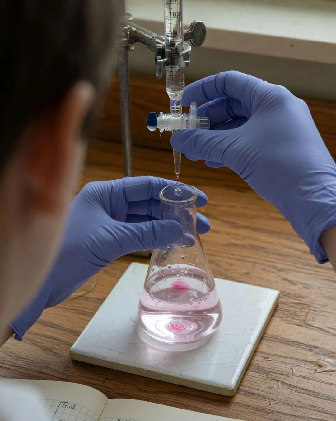 A burette delivering titrant into a conical flask over a white tile, the solution caught mid color-change at the endpoint.